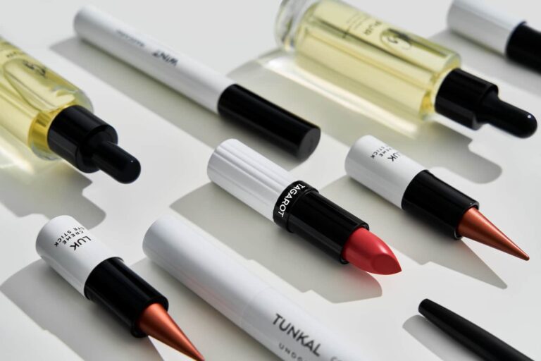 Nahaufnahme von verschiedenen UND GRETEL Kosmetikprodukten, darunter TAGAROT Lippenstift, LUK Creme-Augenstifte und Flaschen mit Öl oder Serum, in einer diagonalen Anordnung.